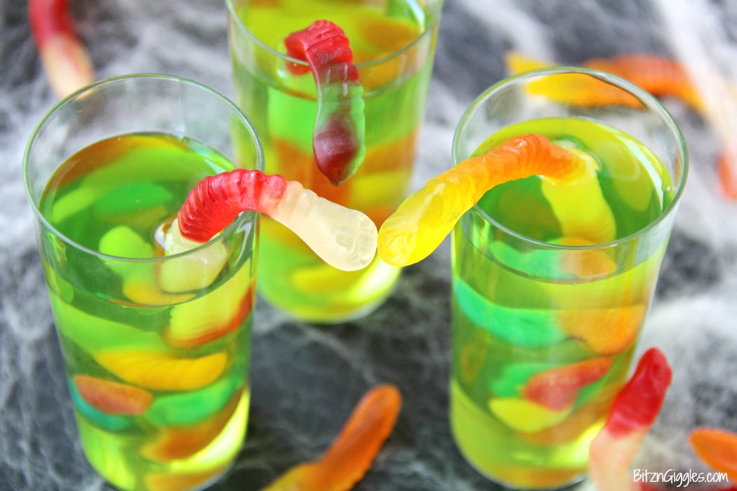 Gummy Worm Jello Shooters - A fun kids treat perfect for mad scientist parties and Halloween! Gummy worms are suspended in green jello and the treat is garnished with a full size worm "crawling" out of the glass!