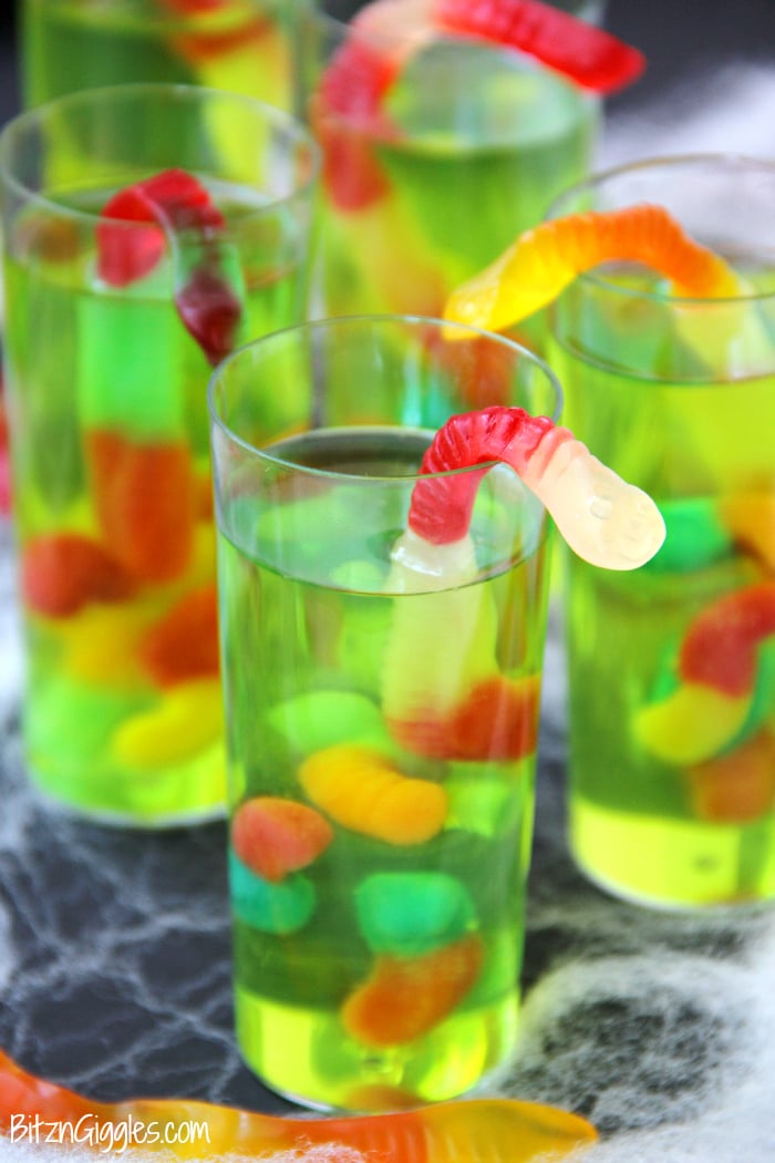 Gummy Worm Jello Shooters - A fun kids treat perfect for mad scientist parties and Halloween! Gummy worms are suspended in green jello and the treat is garnished with a full size worm "crawling" out of the glass!