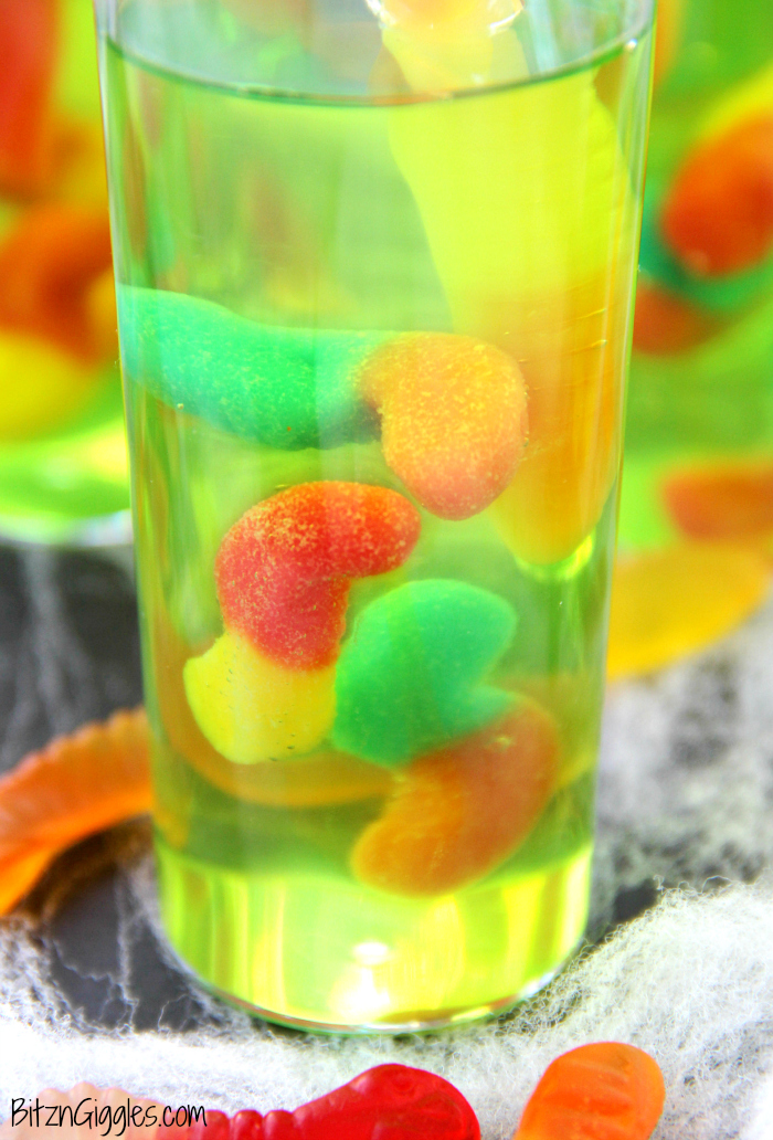 Gummy Worm Jello Shooters - A fun kids treat perfect for mad scientist parties and Halloween! Gummy worms are suspended in green jello and the treat is garnished with a full size worm "crawling" out of the glass!