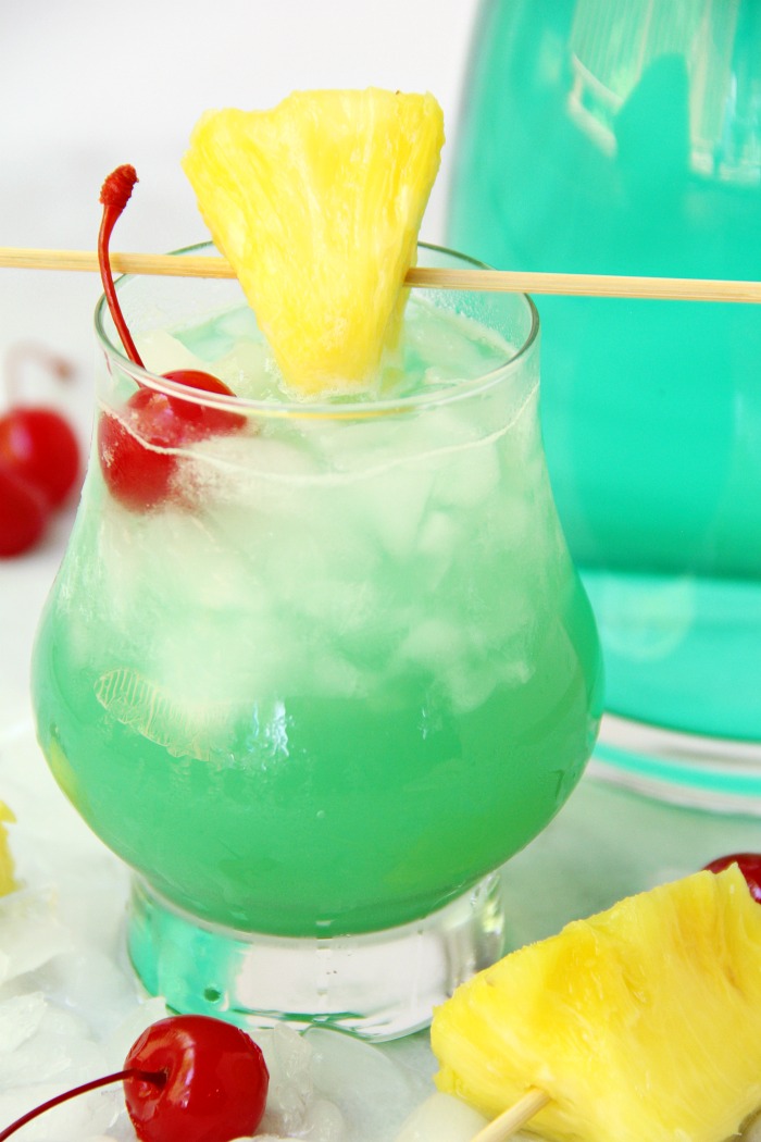 Green Hawaiian cocktail in a glass garnished with a wedge of pineapple and cherries.