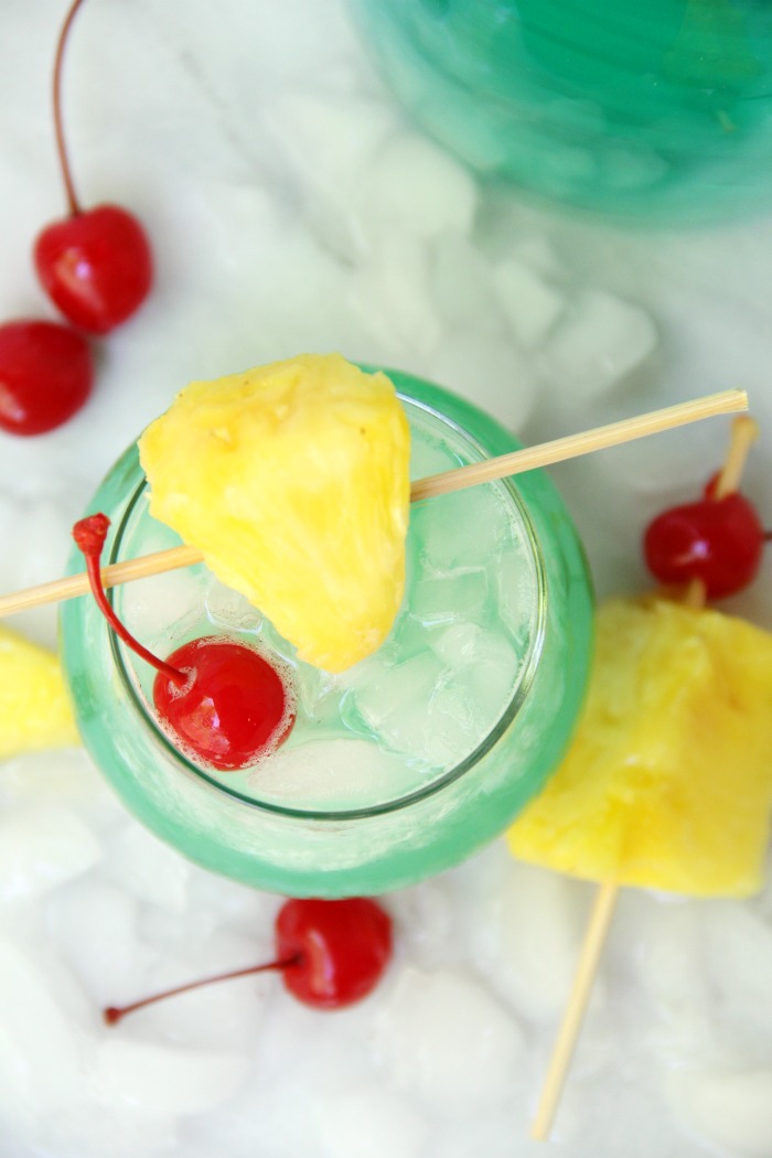 Top down view of green Hawaiian cocktail topped with pineapple slice and cherry.