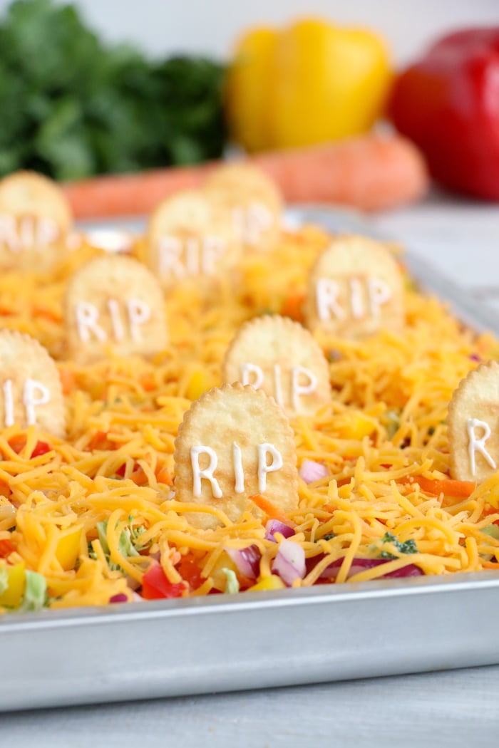 Halloween Veggie Pizza - A spooky themed graveyard pizza featuring a flavorful ranch cream cheese covered crust, topped with colorful veggies and "tombstone" crackers. 