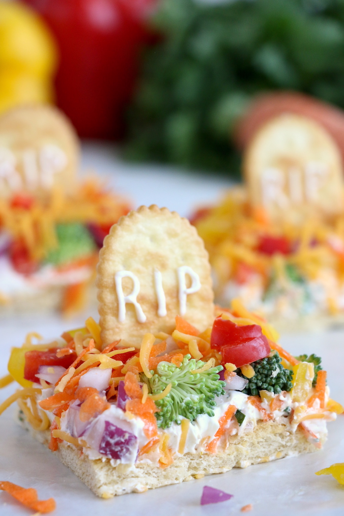 Halloween Veggie Pizza - A spooky themed graveyard pizza featuring a flavorful ranch cream cheese covered crust, topped with colorful veggies and "tombstone" crackers. 