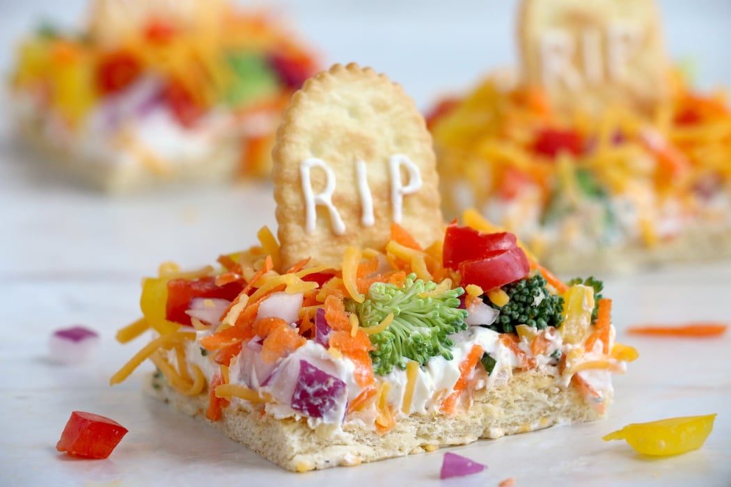 Halloween Veggie Pizza - A spooky themed graveyard pizza featuring a flavorful ranch cream cheese covered crust, topped with colorful veggies and "tombstone" crackers. 