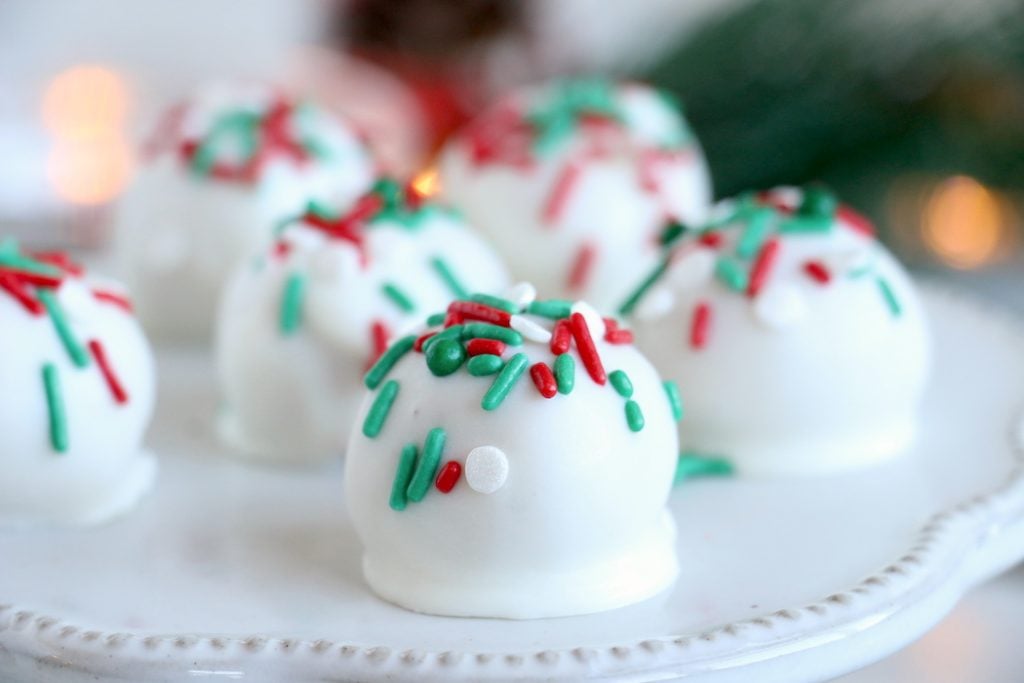 White truffles with red and green sprinkles on a white cake stand.