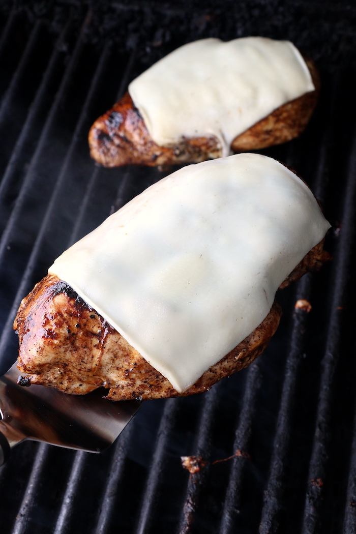 chicken breasts on the grill covered with mozzarella cheese slices