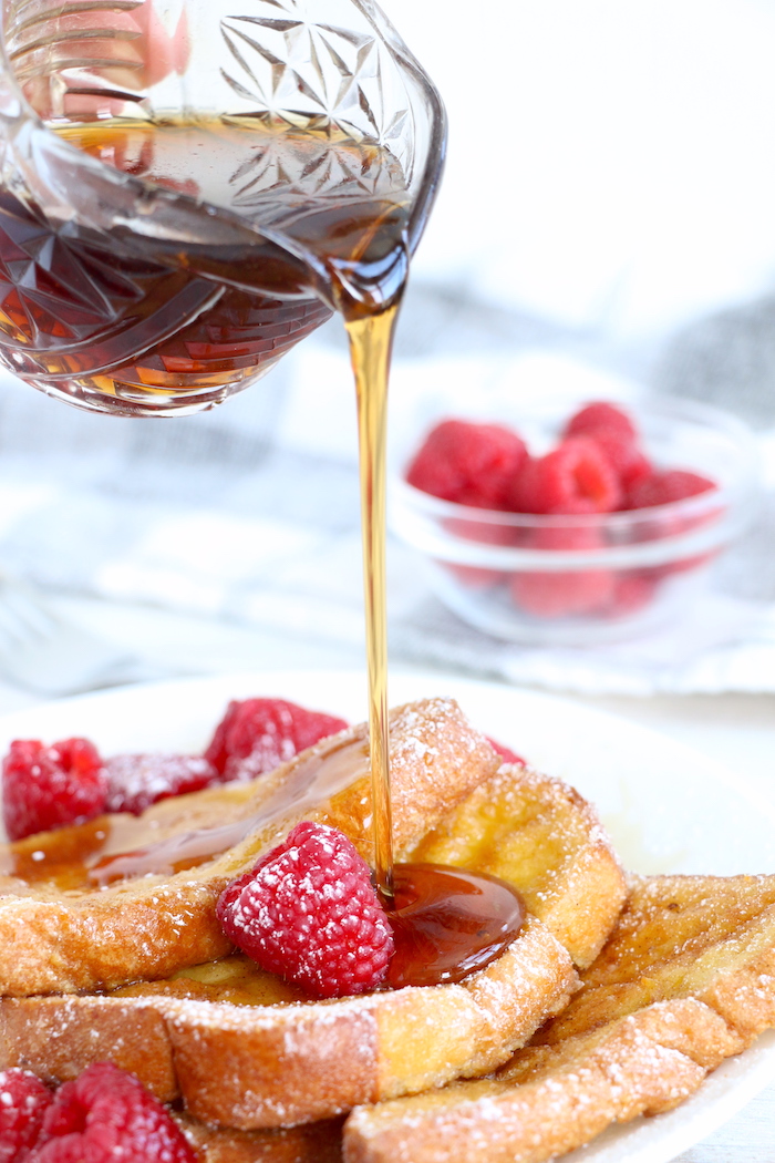 pouring maple syrup on top of French toast with berries and powdered sugar