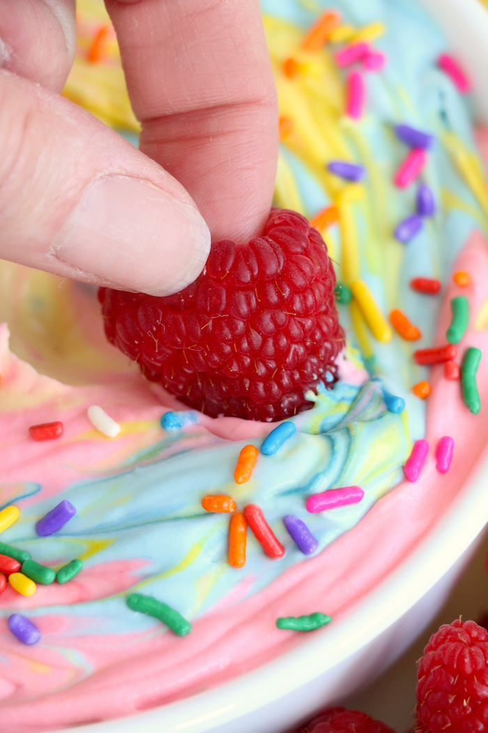 Dipping a strawberry into swirled rainbow fruit dip