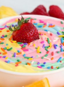 Rainbow fruit dip in bowl with sprinkles and a strawberry