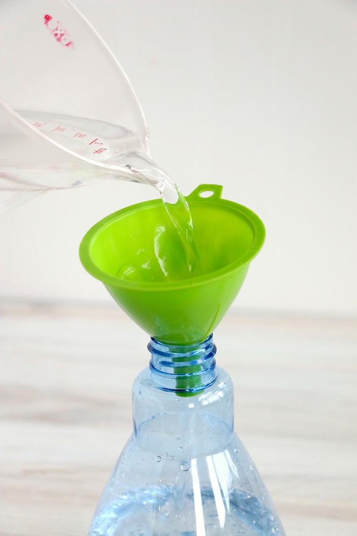 pouring water from a measuring cup into a green funnel