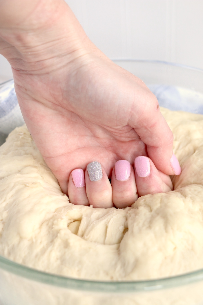 A hand punching bread dough down 