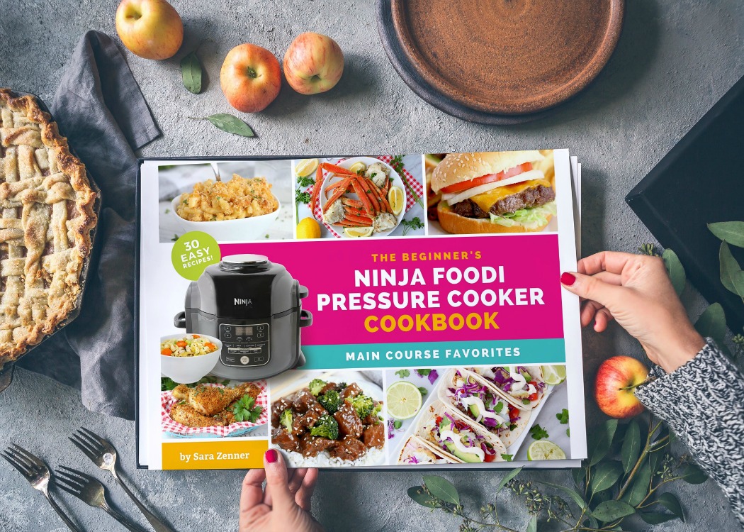 Hands holding Ninja Foodi cookbook above a table