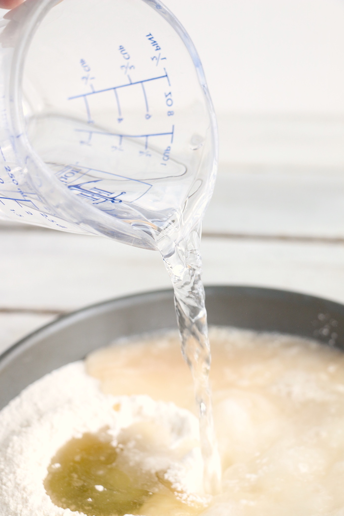 measuring cup pouring water onto cake in pan