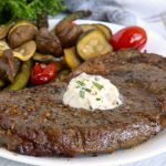 Steak with garlic butter and vegetables in the background
