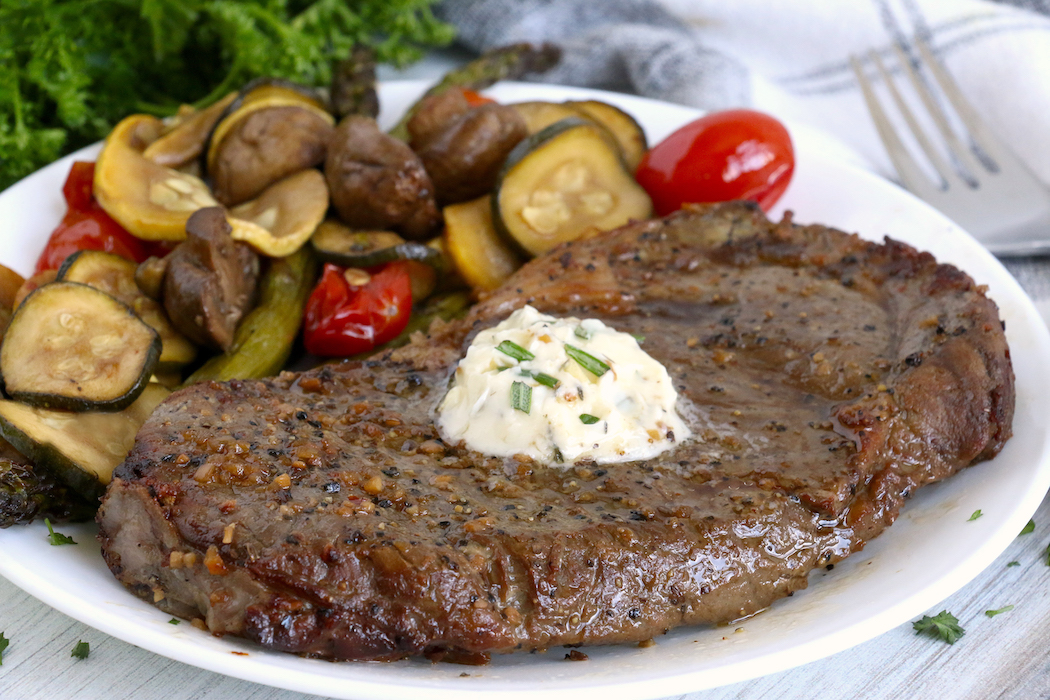Steak with garlic butter and vegetables in the background