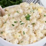 potato salad in white bowl with wooden spoon