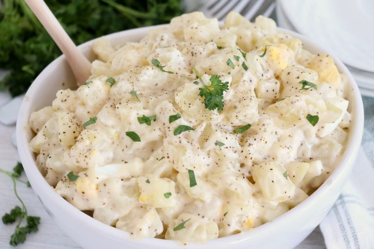 potato salad in white bowl with wooden spoon