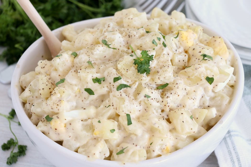 potato salad in white bowl with wooden spoon