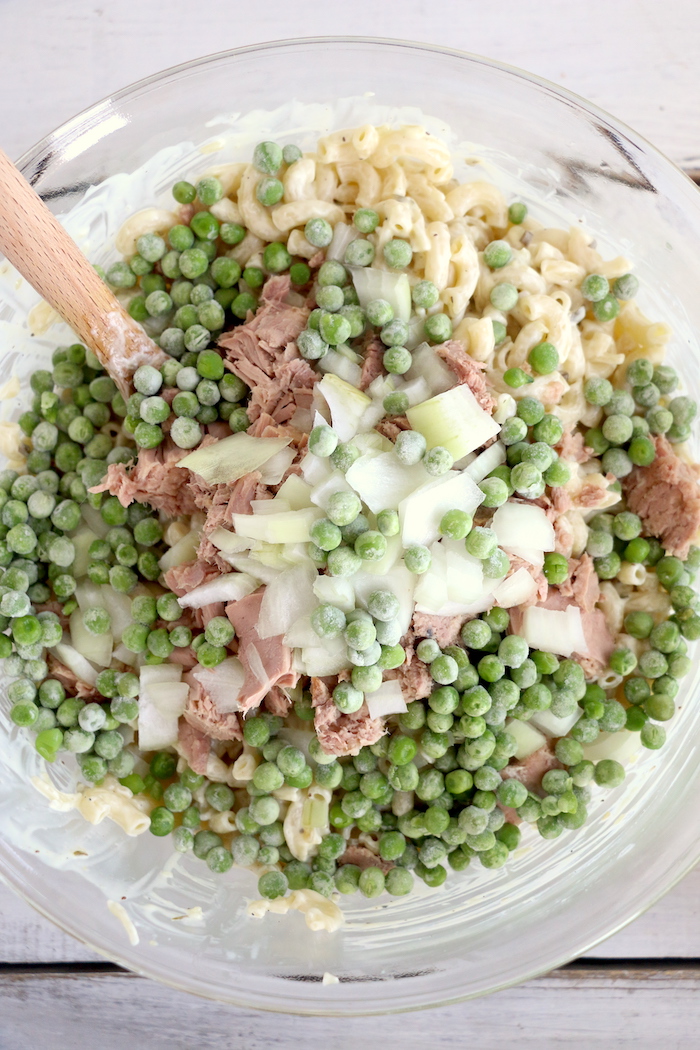 adding in peas, tuna and onions to pasta salad