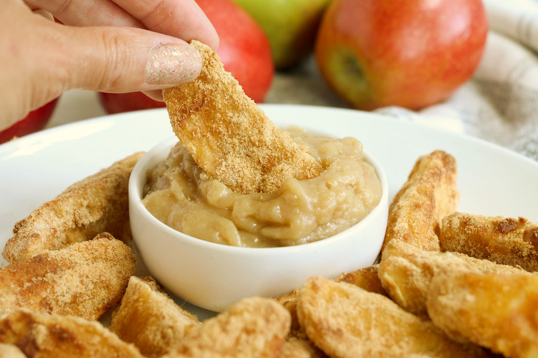 hand dipping air fried apple wedge in caramel