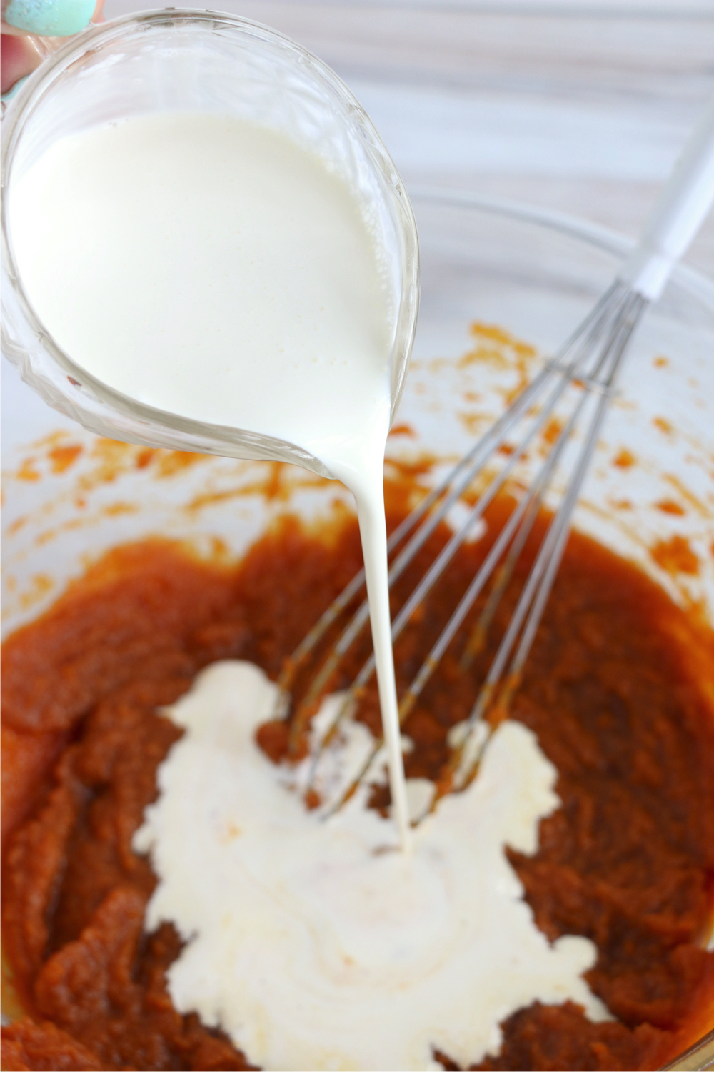 adding heavy cream to pumpkin mixture in mixing bowl