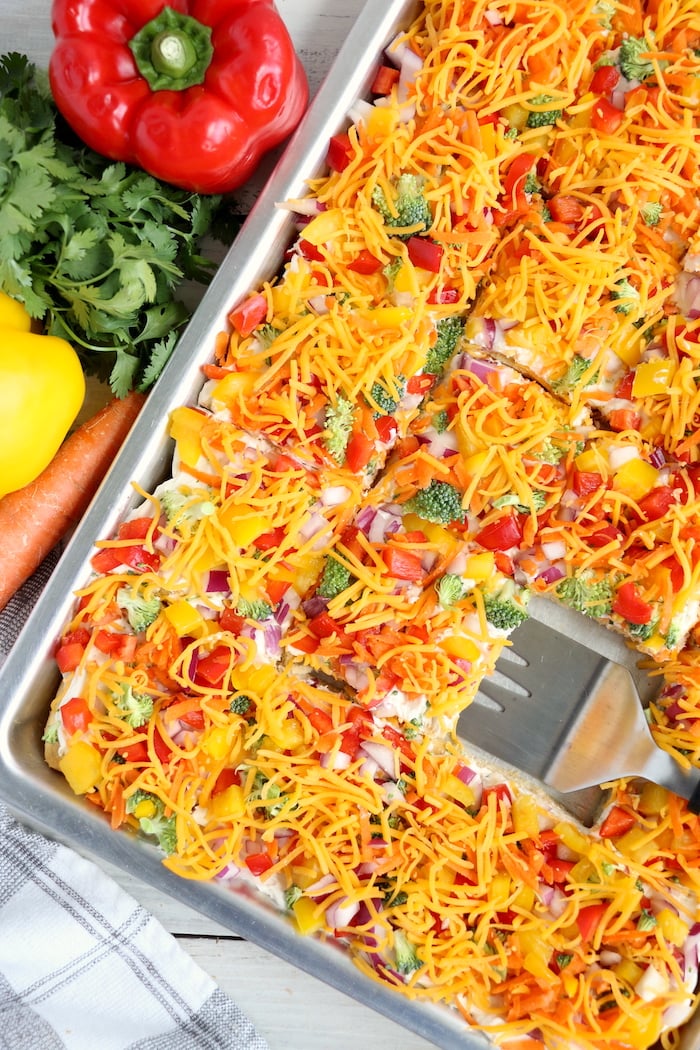 using a spatula to remove a piece of veggie pizza from the pan