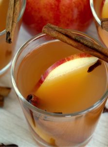 glass of apple cider garnished with apple slices and cinnamon sticks