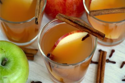 glass of apple cider garnished with apple slices and cinnamon sticks