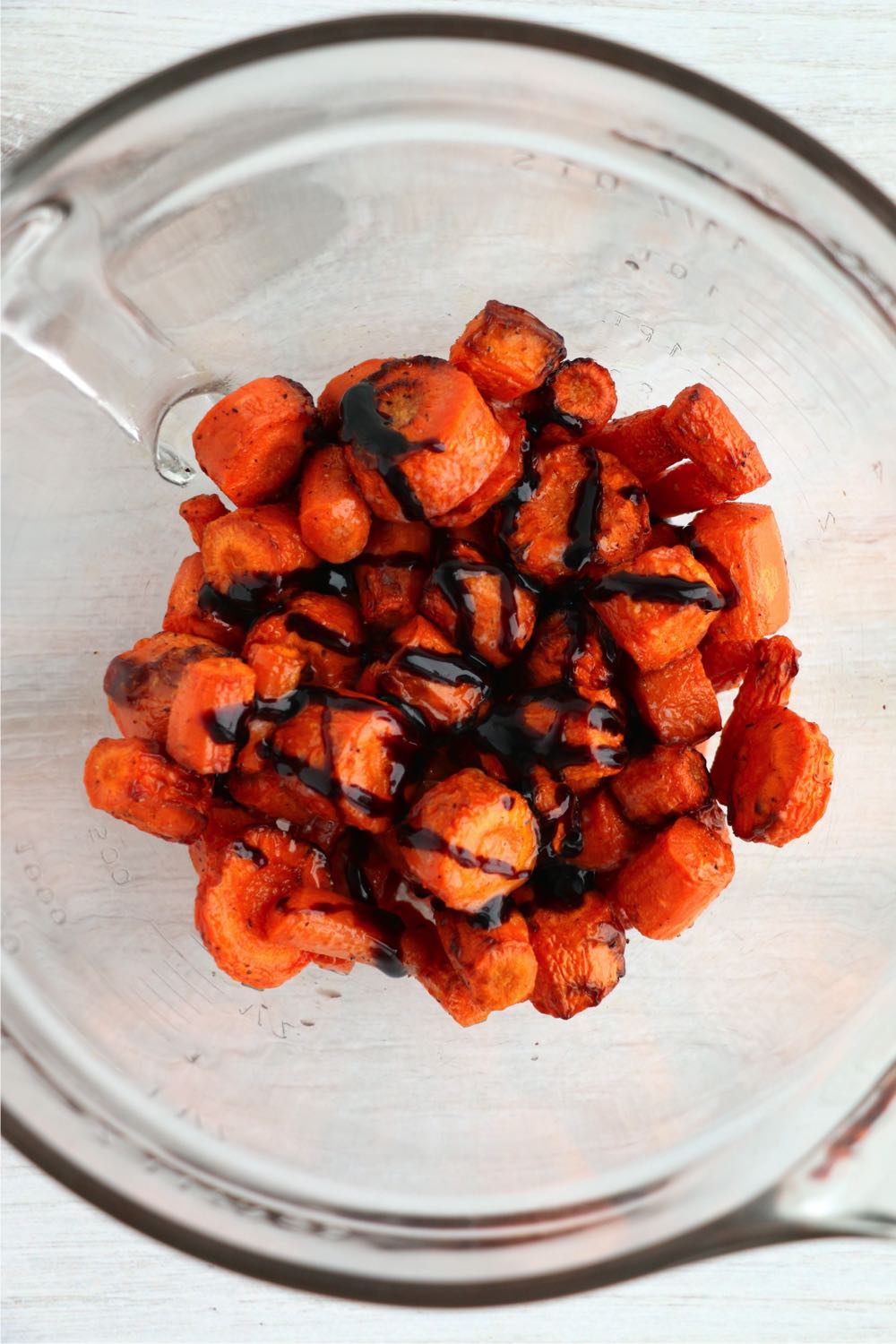 Tossing roasted carrots in a bowl with balsamic glaze