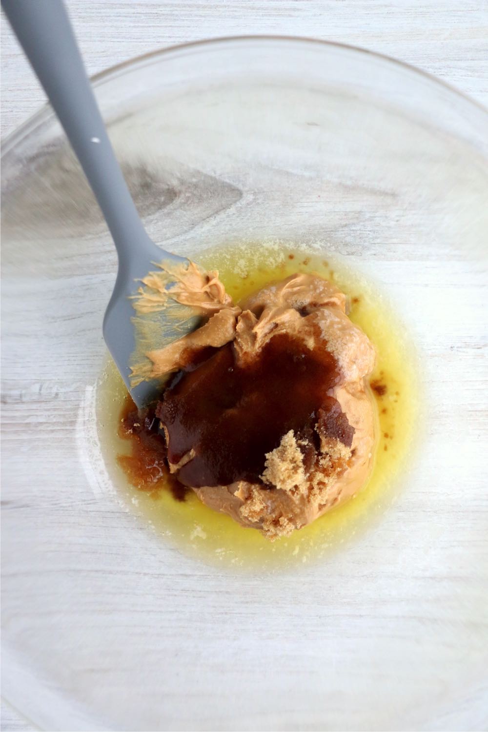 A mixing bowl with peanut butter, melted butter, brown sugar, vanilla and a dash of salt