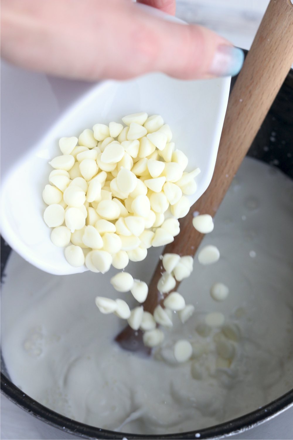pouring white chocolate chips into stock pot filled with milk