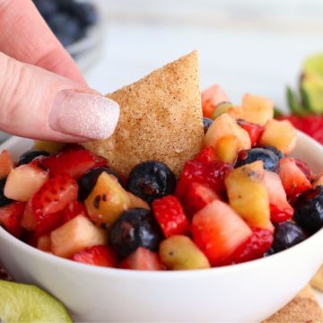 dipping a chip in a white bowl filled with fruit salsa