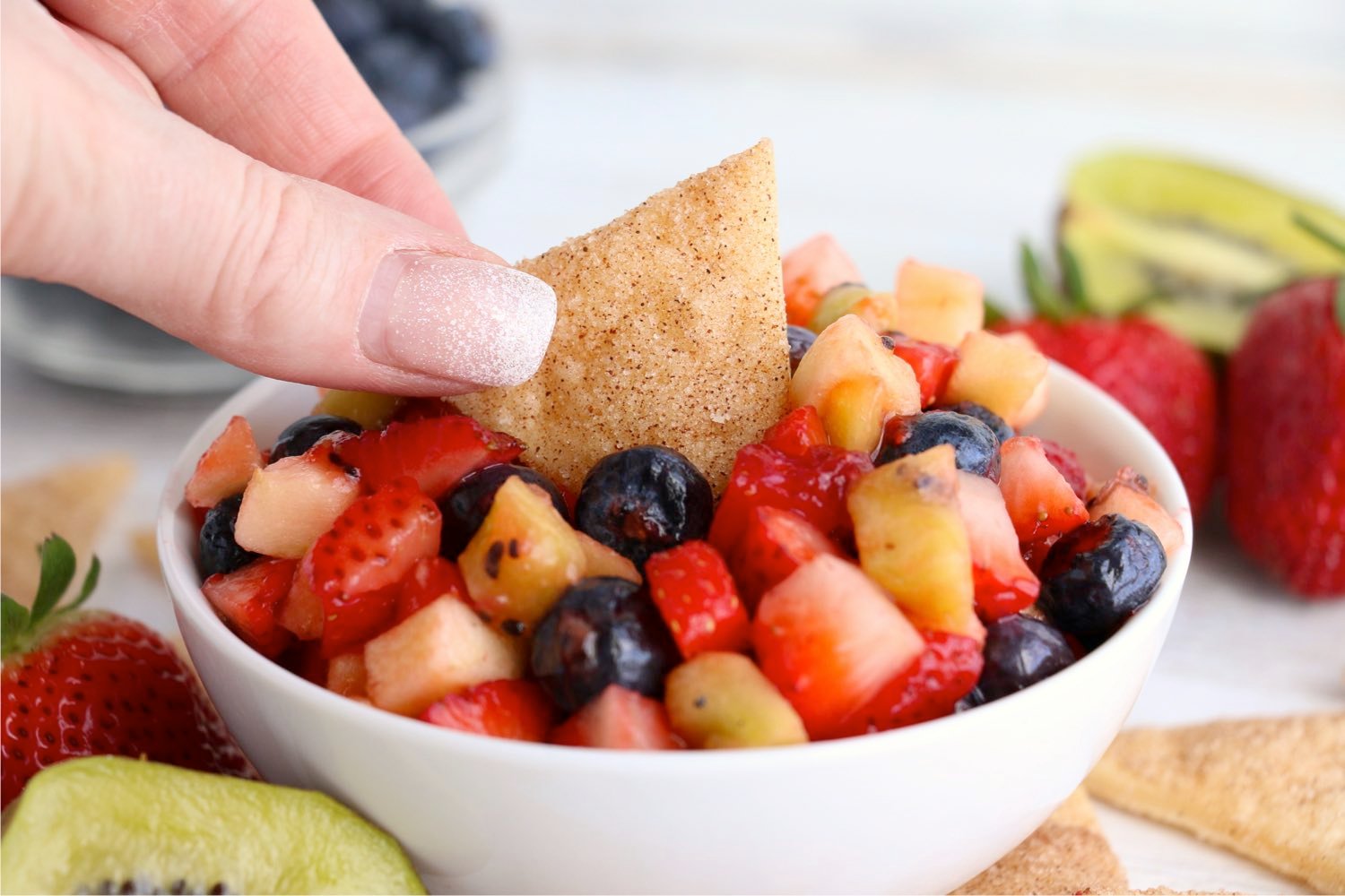 dipping a chip in a white bowl filled with fruit salsa