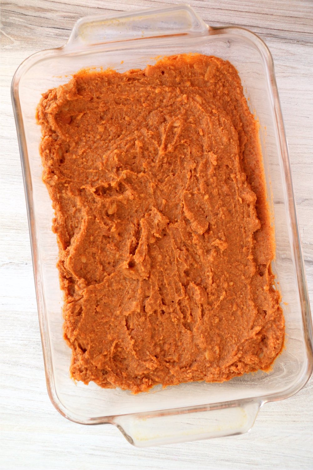 refried beans spread on the bottom of a glass dish
