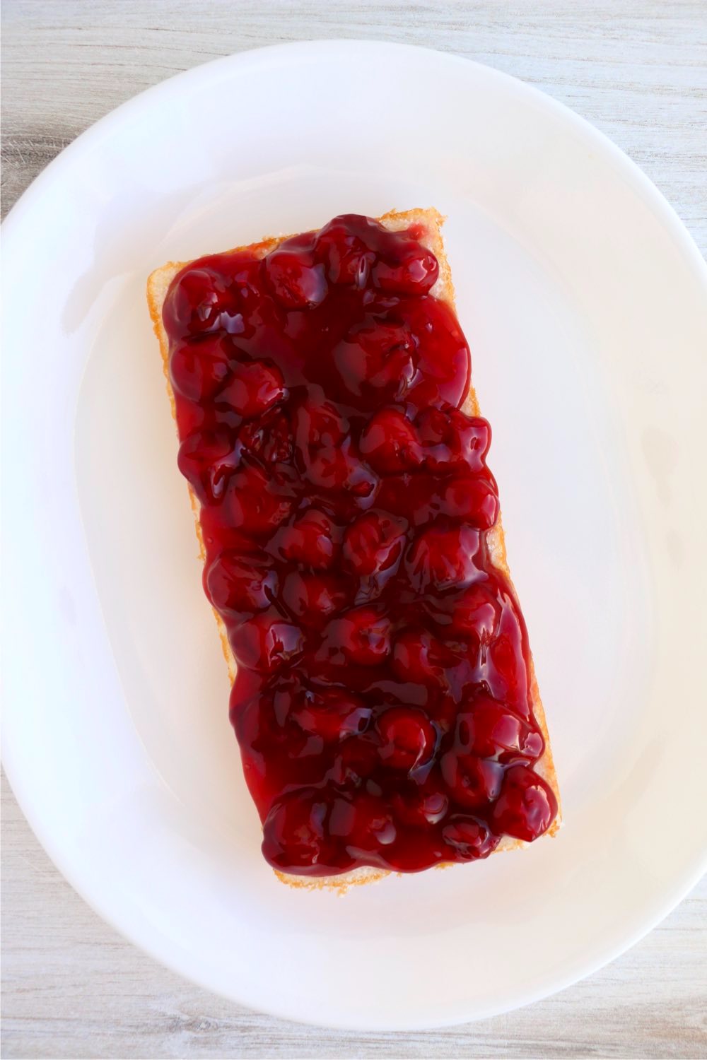 Layer of pound cake on white plate covered with canned cherries