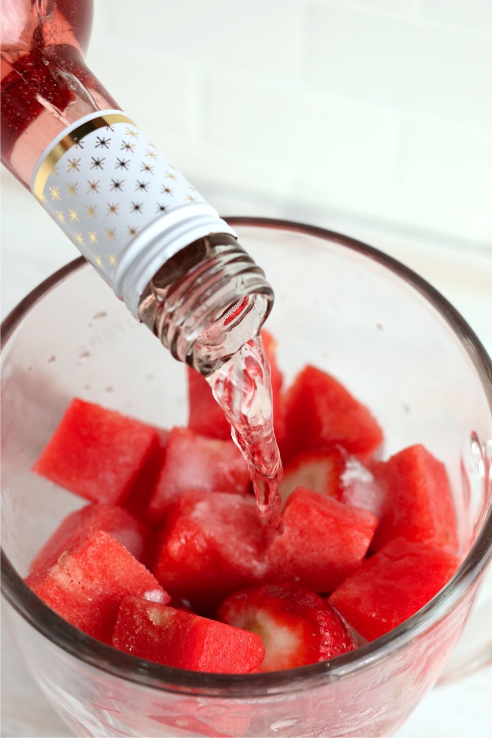 Adding wine to a blender filled with watermelon and strawberries
