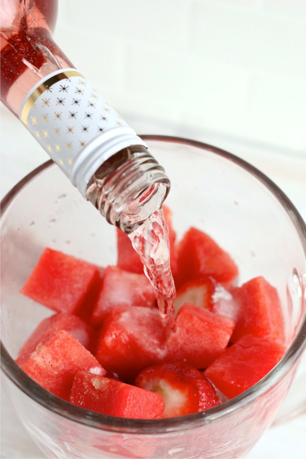 Adding wine to a blender filled with watermelon and strawberries