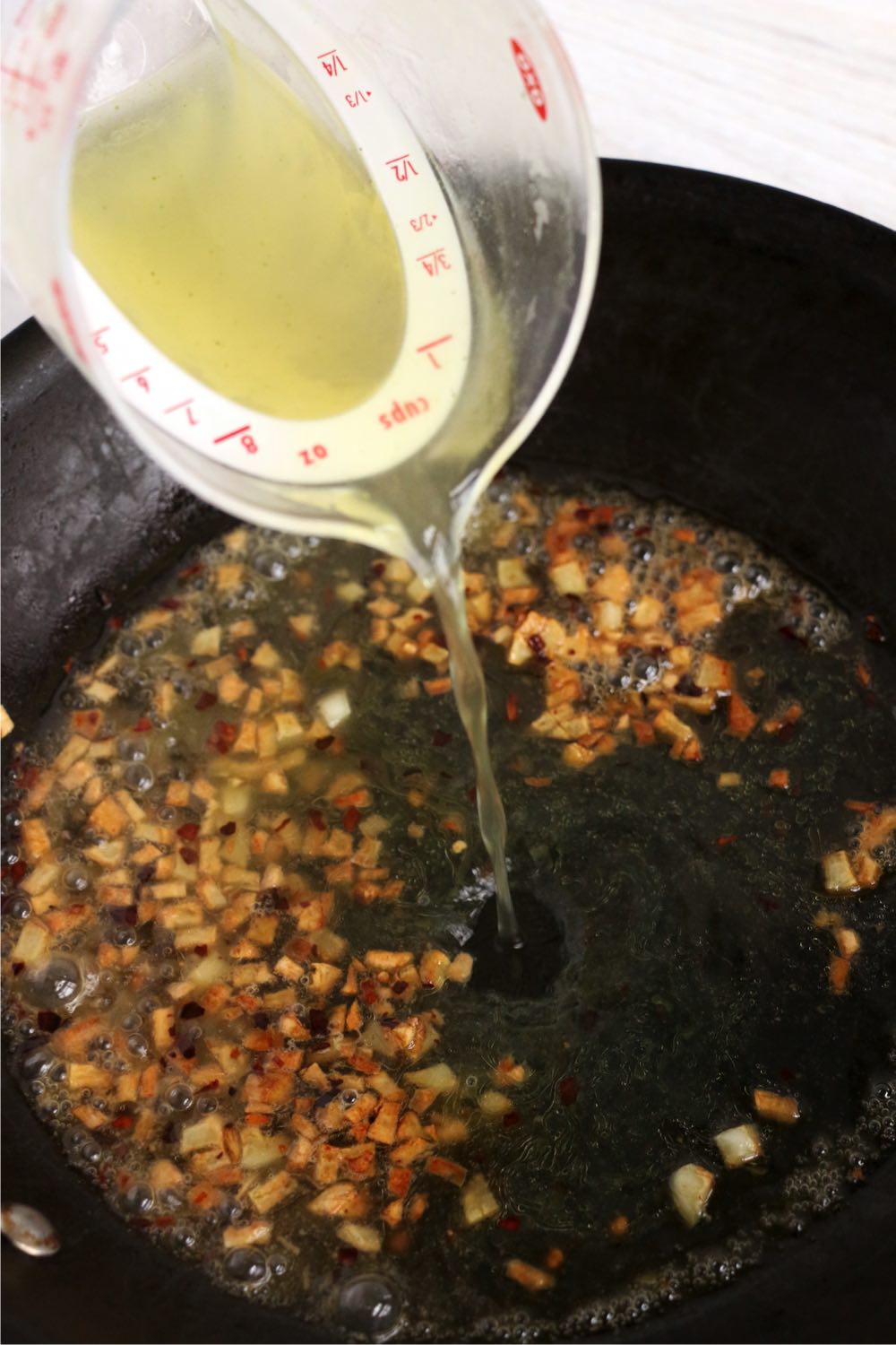 Adding chicken stock to garlic and red pepper flakes