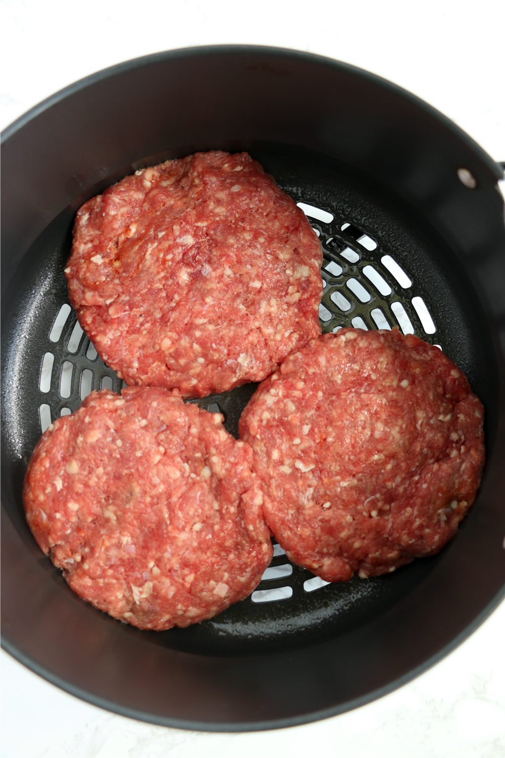 three burgers placed into Ninja Foodi air crisp basket