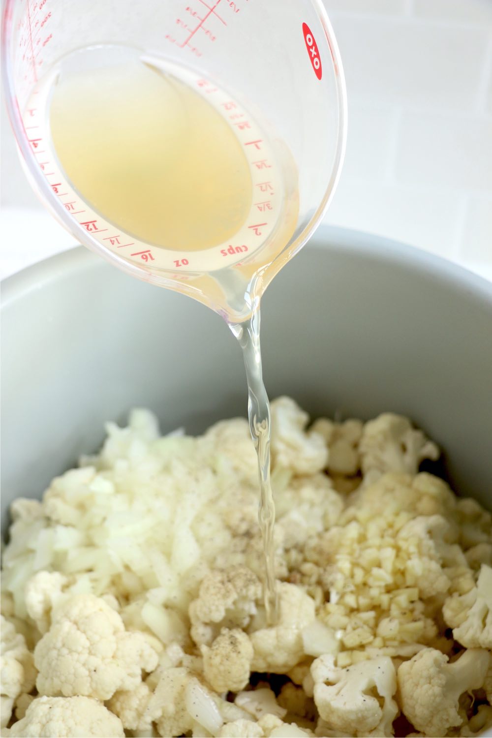 pouring chicken broth into Ninja Foodi cooking pot filled with cauliflower