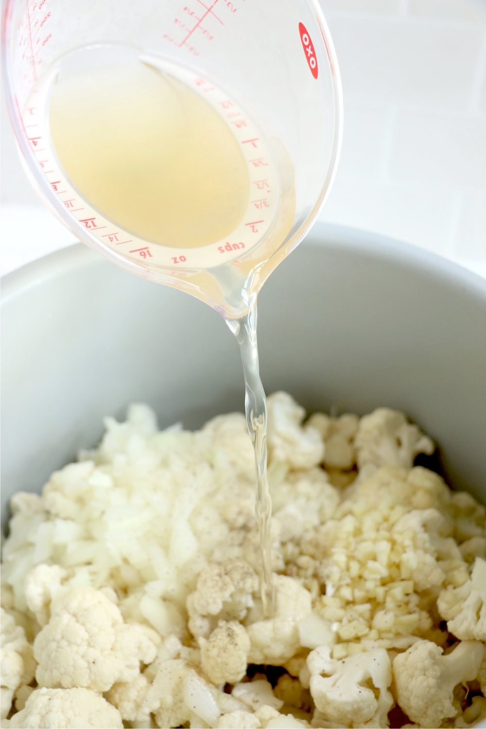 pouring chicken broth into Ninja Foodi cooking pot filled with cauliflower