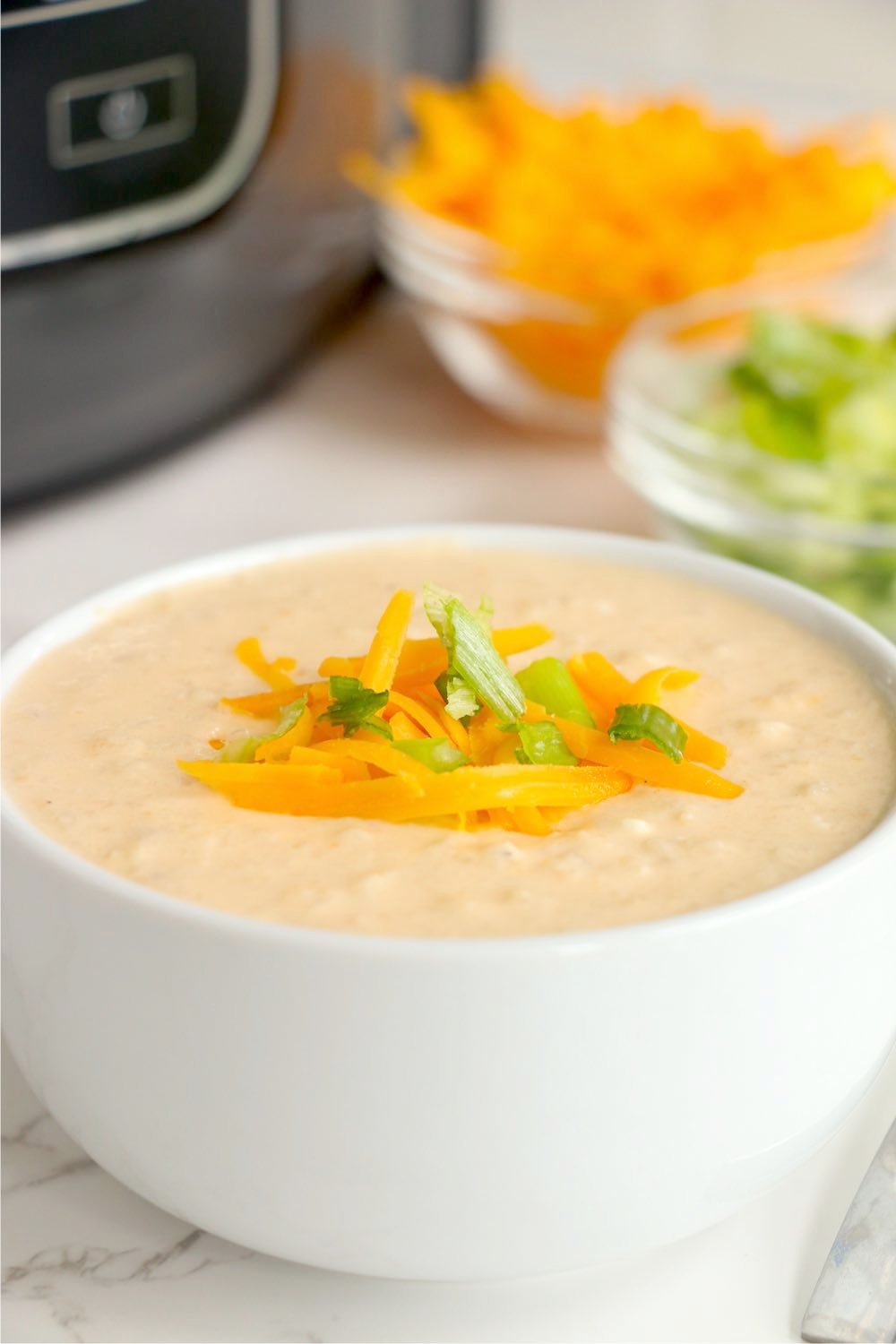 bowl of cheesy cauliflower soup garnished with shredded cheese and green onions