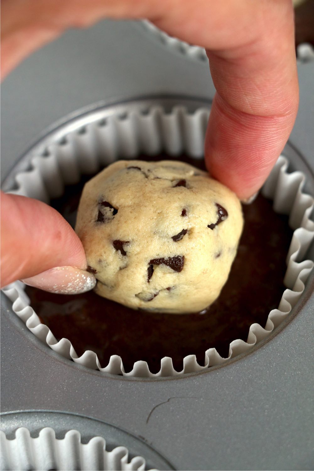 placing a ball of cookie dough on top of a cupcake