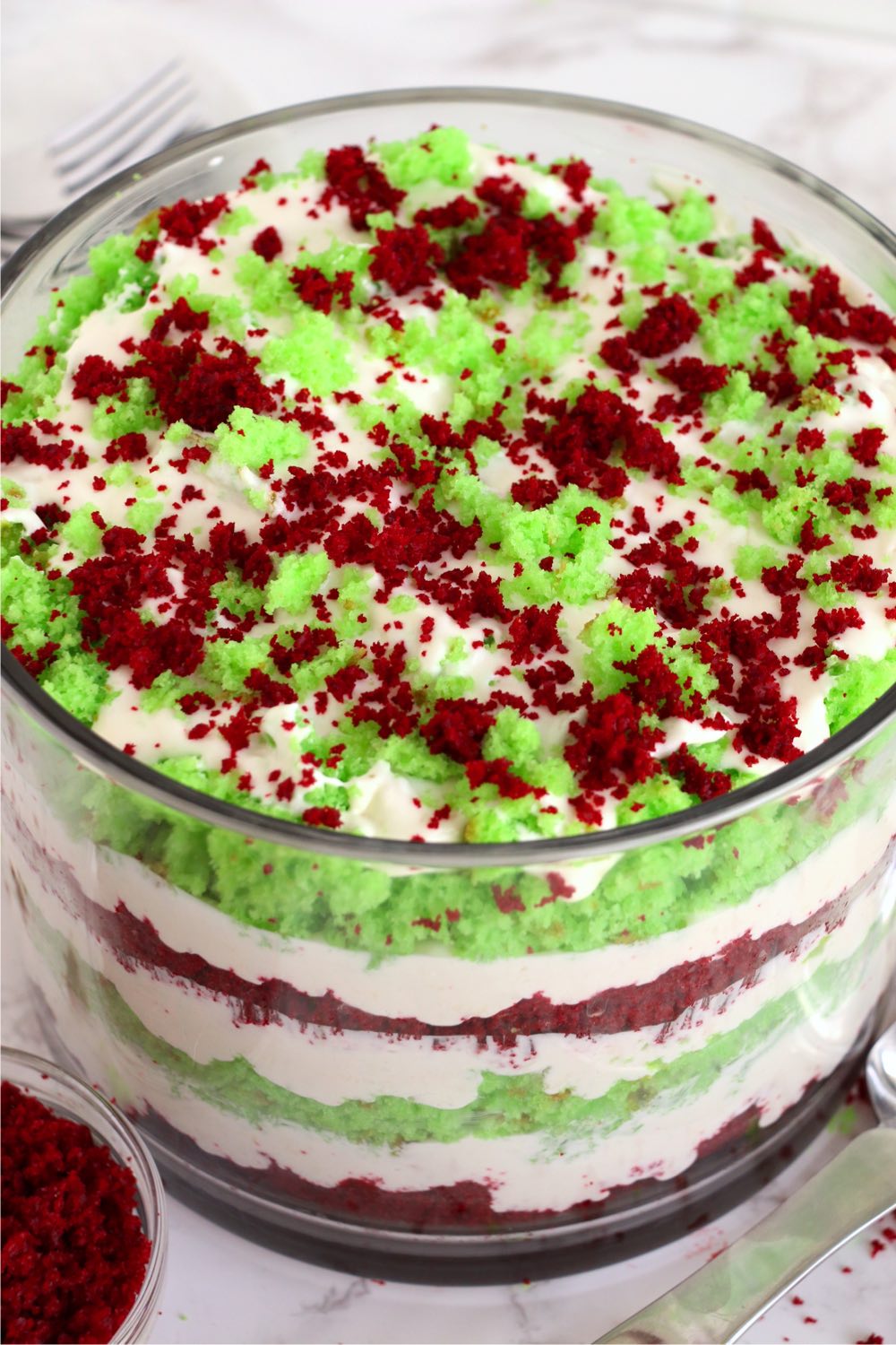 Glass trifle bowl filled with red and green cake crumbles and cream.