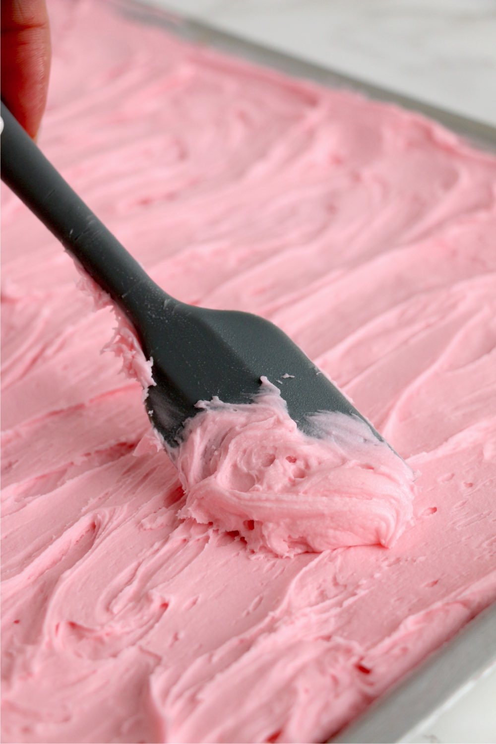 spreading pink frosting on cake bars