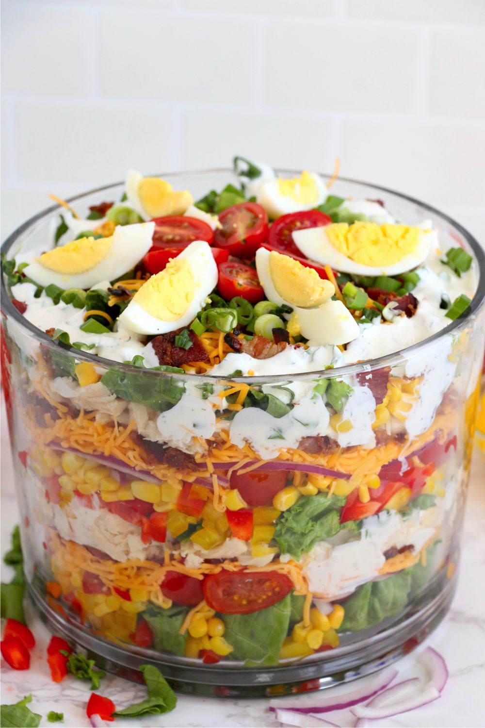 trifle bowl filled with vegetables, lettuce and dressing