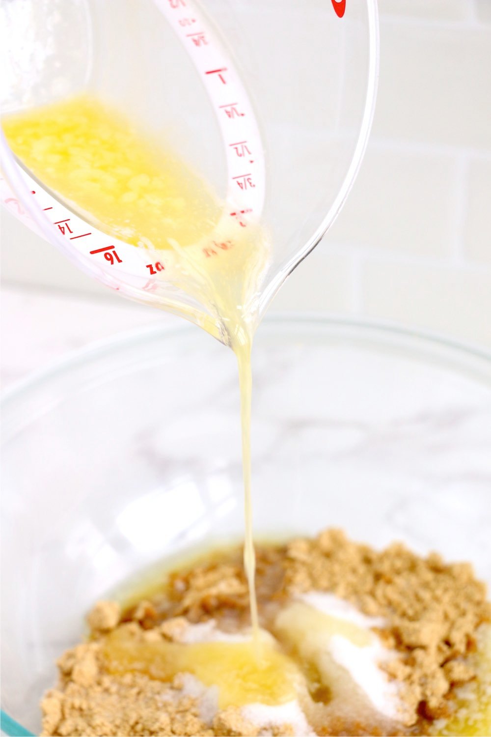 adding butter to a bowl of crushed graham crackers