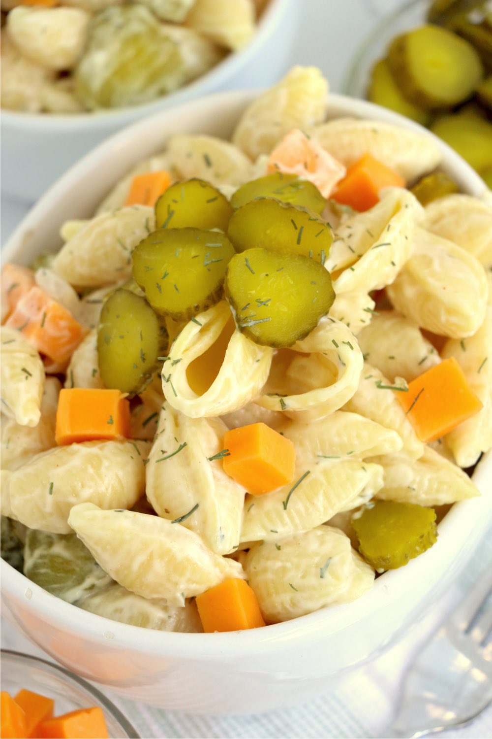 close up of white bowl with pasta salad and sliced pickles