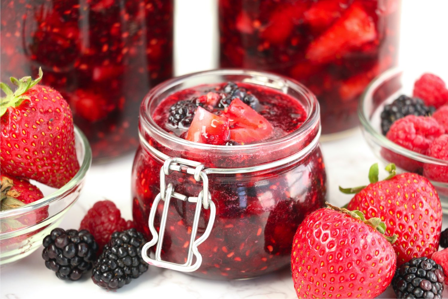 open jar of jam surrounded by fresh berries