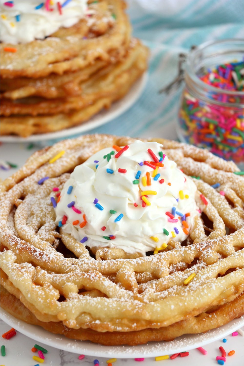 Funnel cakes topped with whipped cream with sprinkles in background